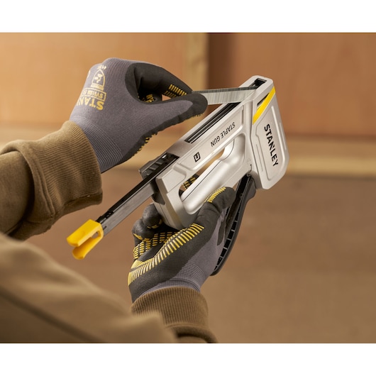 Stanley STHT70150-0 staple gun in use, gloved hands loading staples into silver tool, close-up photo.