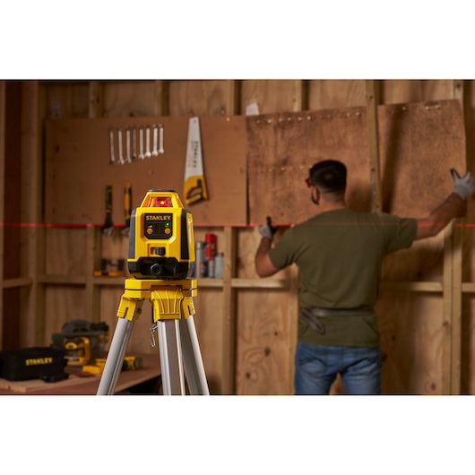 STANLEY STHT77616-0 laser level on tripod projects red line in workshop with person aligning boards.