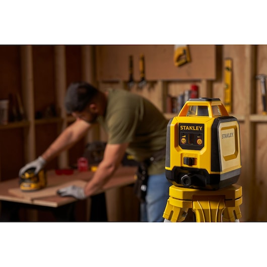 STANLEY STHT77616-0 laser level on tripod in workshop, person working in background.