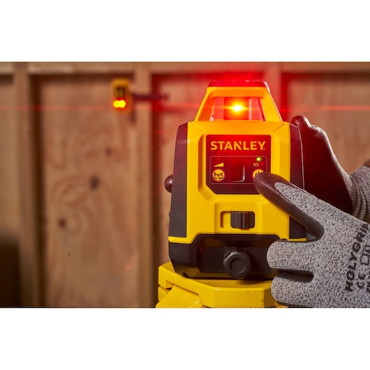 STANLEY STHT77616-0 laser level on tripod, activated by gloved hand in workshop setting.