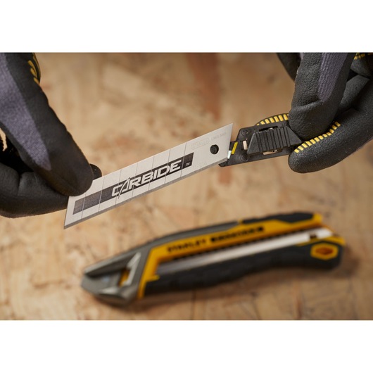STANLEY STHT8-11818 utility knife with carbide blade close-up, gloves holding blade, yellow and black handle visible.