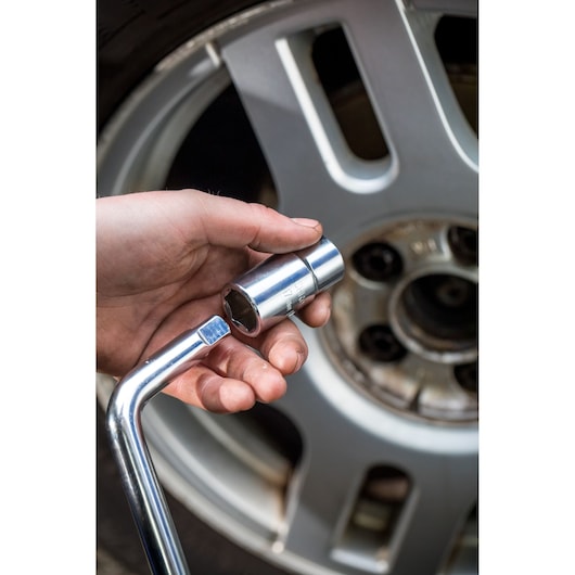 STANLEY STHT80890-0 socket wrench held near car wheel, close-up photo showing tool and metallic finish.