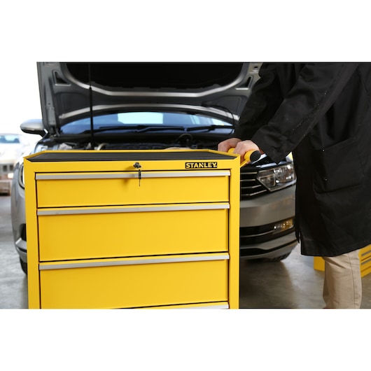 Stanley STMT1-75063 yellow tool chest with four drawers, photographed in a garage setting next to a car.