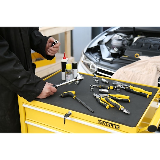 STANLEY STMT1-75063 tool assortment with yellow handles on top of tool chest, mechanic holding socket.