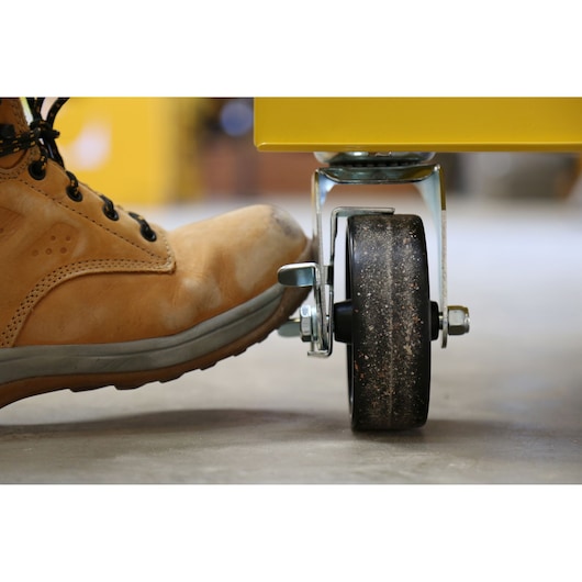 STANLEY STMT1-75063 photography of boot pressing locking lever on heavy-duty caster wheel.