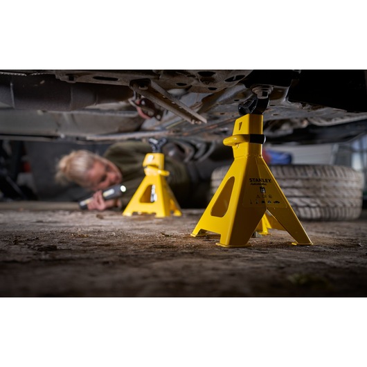 Photo of STANLEY STMT81255-1 yellow automotive jack stands supporting a car, mechanic working underneath.