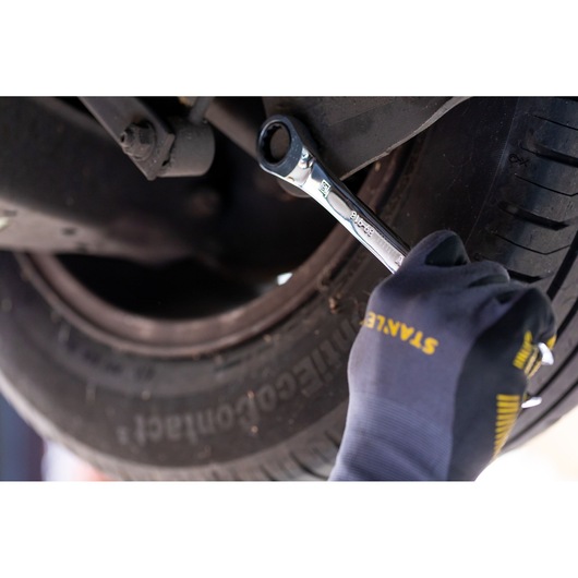 STANLEY STMT82847-0 wrench used on car wheel by gloved hand in close-up automotive context.