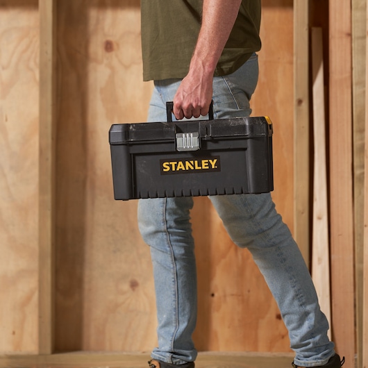 Photo of STANLEY STST1-75518-KR black toolbox carried by person in jeans, wooden wall background.