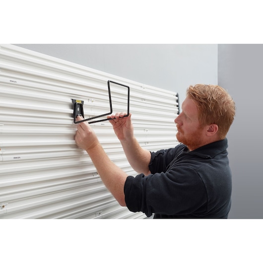 STANLEY STST82604-1 wall mount hook being installed on white slatwall, side angle, for storage organization.