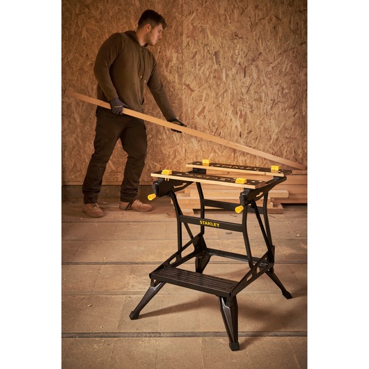 Stanley STST83400-1 folding workbench with yellow clamps in workshop setting, front angle photography.