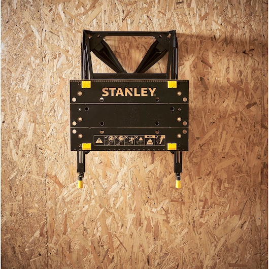 STANLEY STST83400-1 black folding workbench with yellow accents mounted on wooden wall.
