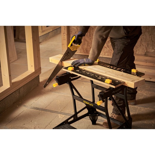 STANLEY STST83400-1 portable workbench with wood clamped, handsaw cutting wood, workshop setting.