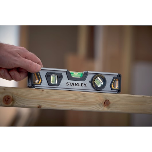 STANLEY XTHT0-42495 spirit level held on wood beam, construction setting, close-up angle.